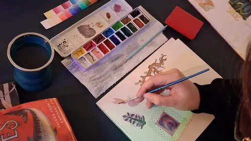 Person painting with watercolors on desk.
