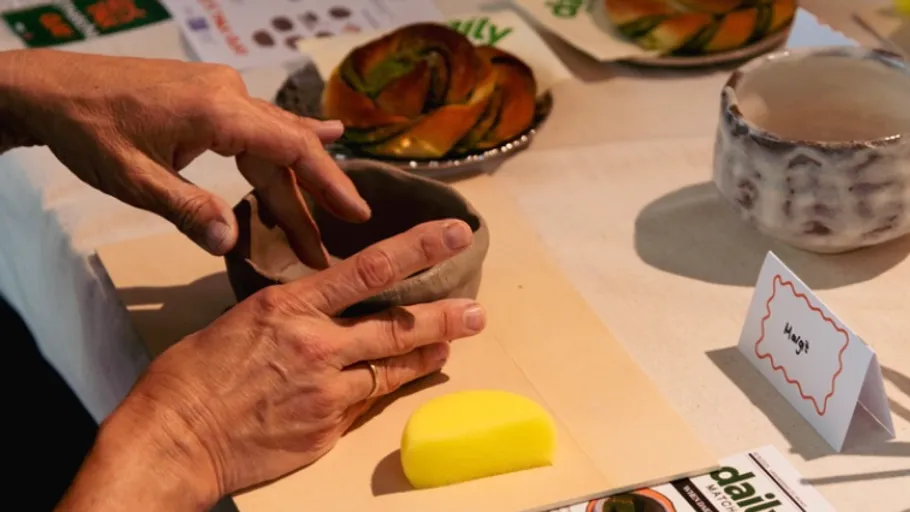 Hands shaping clay bowl on table.