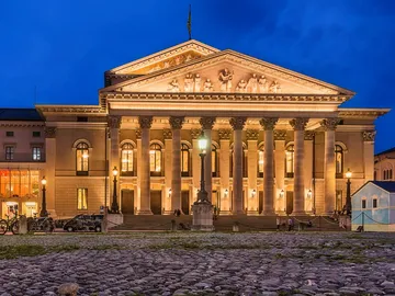 Historisches Gebäude leuchtet nachts vor beleuchtetem Platz.
