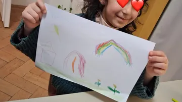 Child holding colorful drawing indoors.