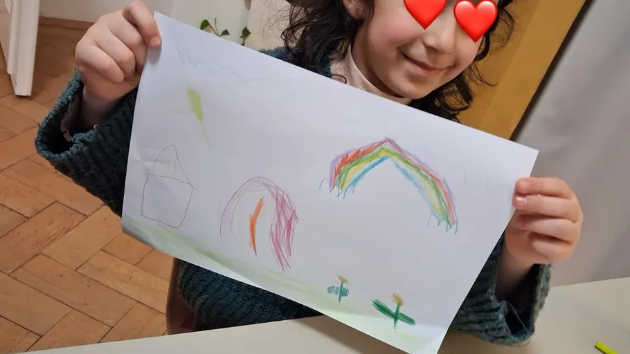 Kind hält farbige Zeichnung am Tisch.