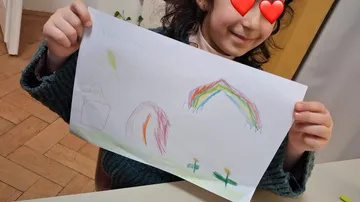 Child holding colorful drawing indoors.
