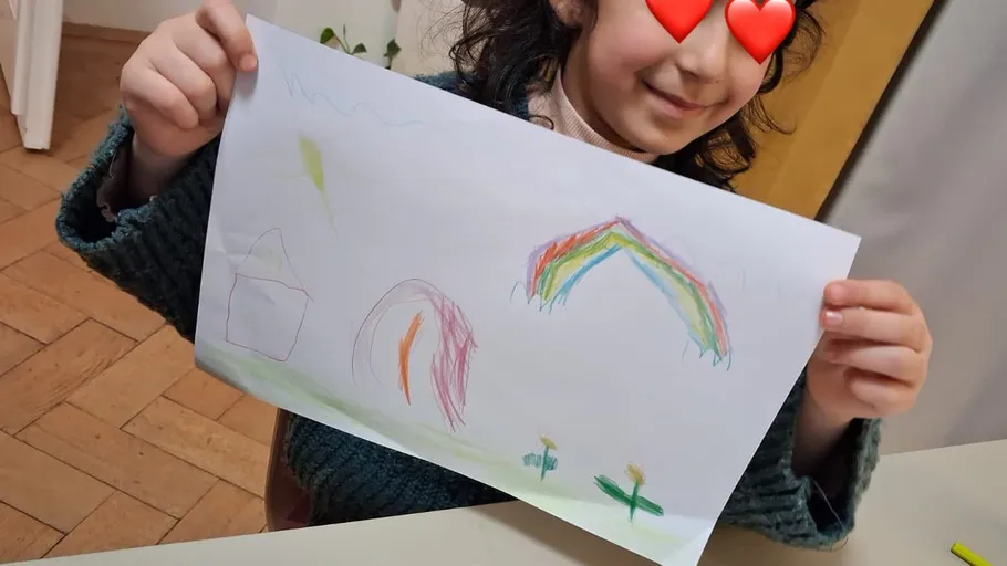 Child holding drawing with colorful rainbow.