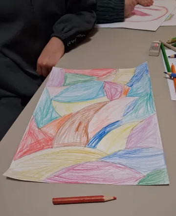 Child drawing abstract shapes with colored pencils.