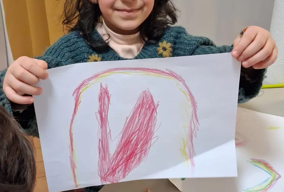 Child holding colorful drawing indoors.