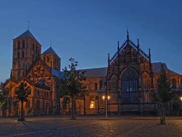 Historic church building illuminated, surrounded by trees and squares.