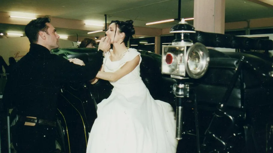 Bride and groom arguing beside classic car.