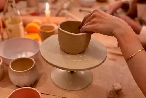 Hand shapes clay bowl on pottery wheel.