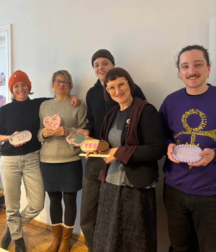 Five people holding decorated heart objects indoors.