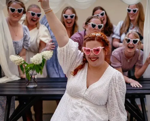 Women wearing heart sunglasses, smiling indoors.