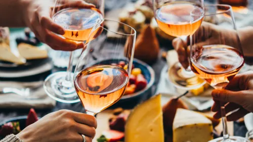 Hände stoßen Weingläser über Tisch an.