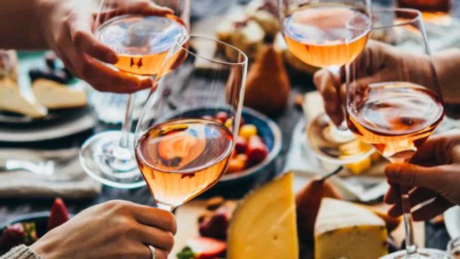 Hands toasting wine glasses over table.