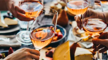 Hände heben Gläser mit Roséwein, festlicher Tisch.