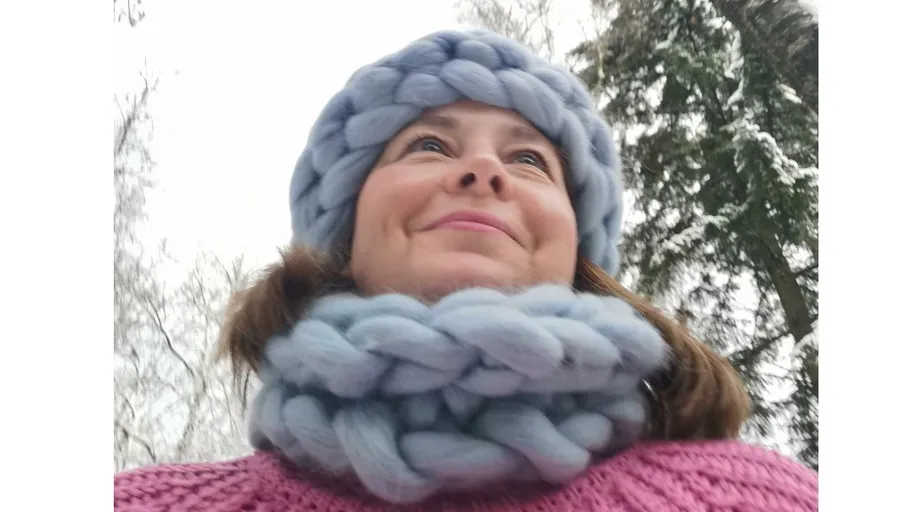 Person wearing knitted hat and scarf outdoors.