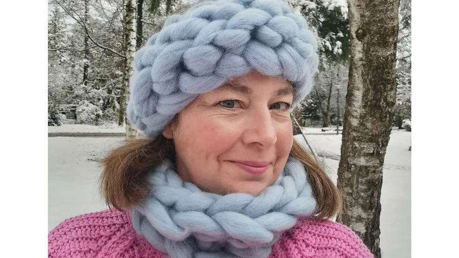 Frau trägt gestrickte Mütze und Schal im verschneiten Wald.