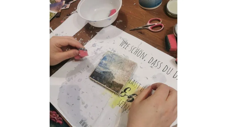 Hands transferring image onto a tile, table setup.