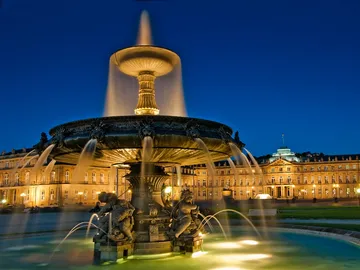 Fountain bubbles water surrounded by illuminated buildings.