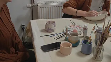 People painting pottery at a table indoors.