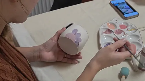 Person painting ceramic cup with brush indoors.