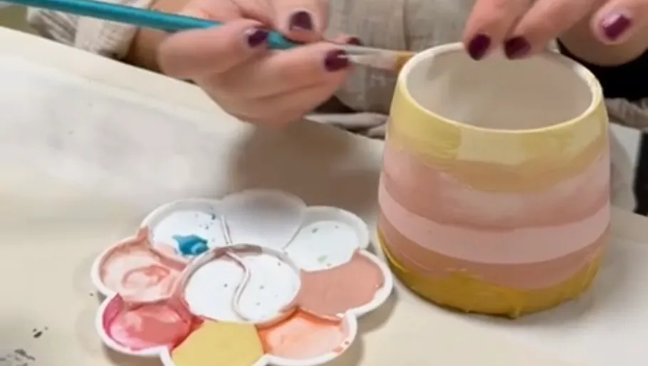 Hand painting colorful ceramic pot at table.
