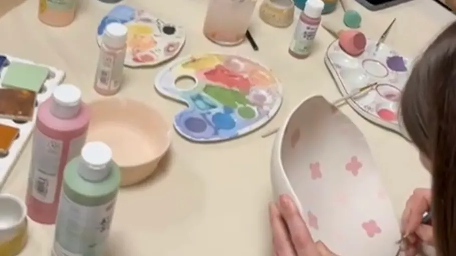 Person bemalt Keramik, umgeben von Farben.