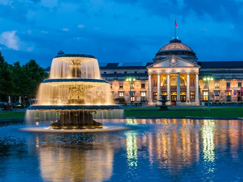 Fountain bubbles, illuminated in front of a historic building at night.