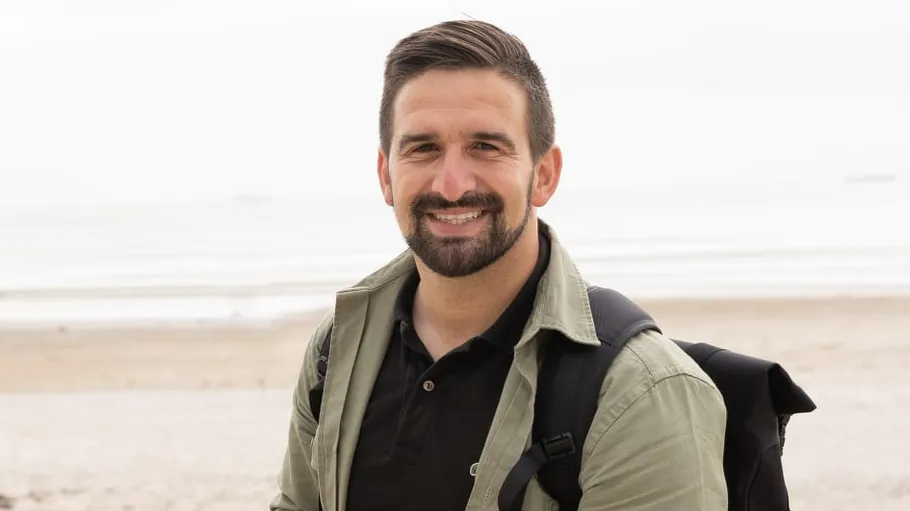 Man smiling with backpack at beach.