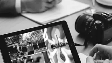 Tablet displaying photos, beside notebook and camera.