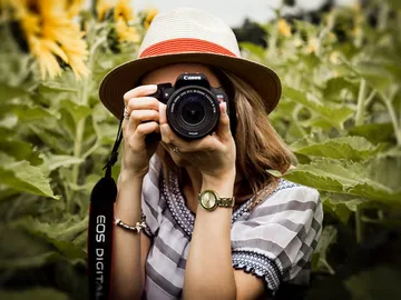 Frau mit Kamera fotografiert in sonnigen Blumenfeld.