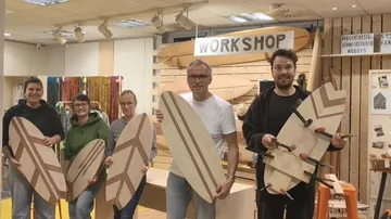 Five people holding wooden boards in workshop.