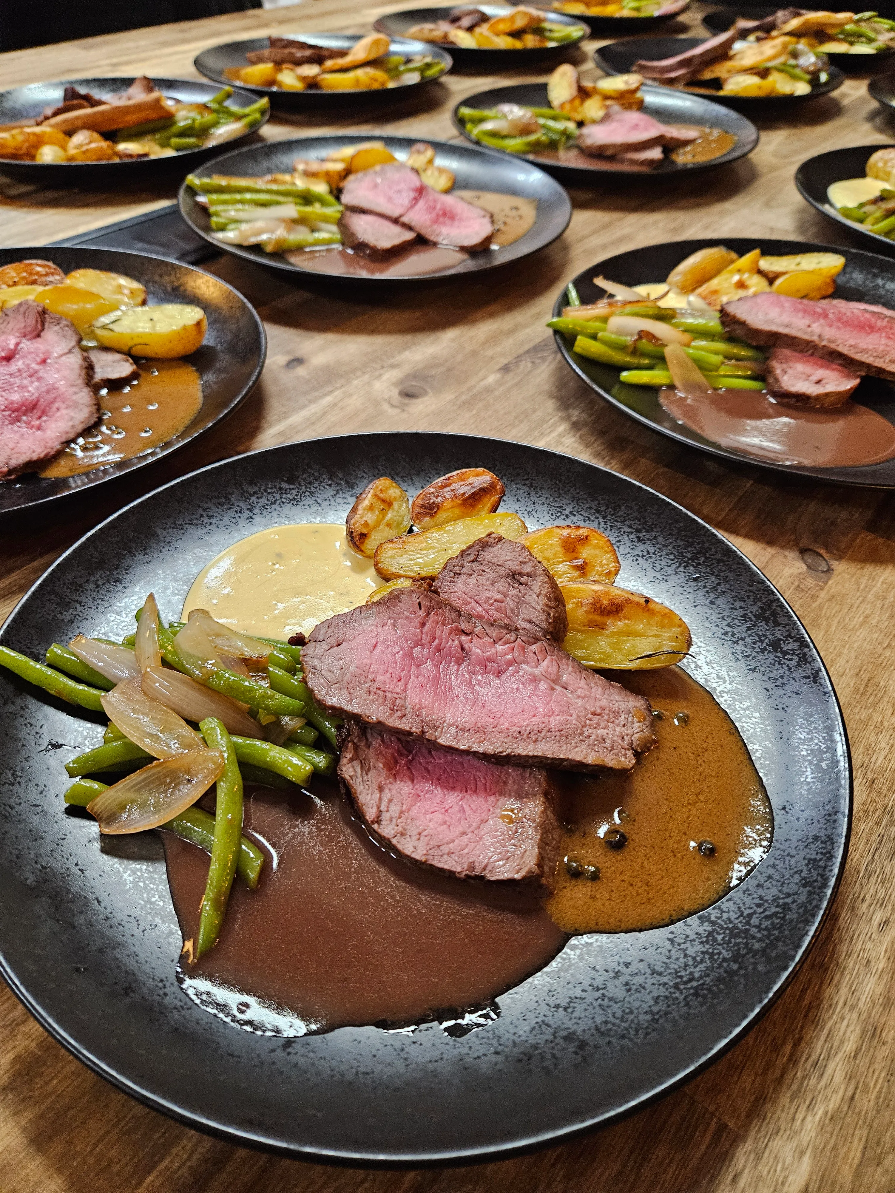 Plates of beef, vegetables, and potatoes on table.