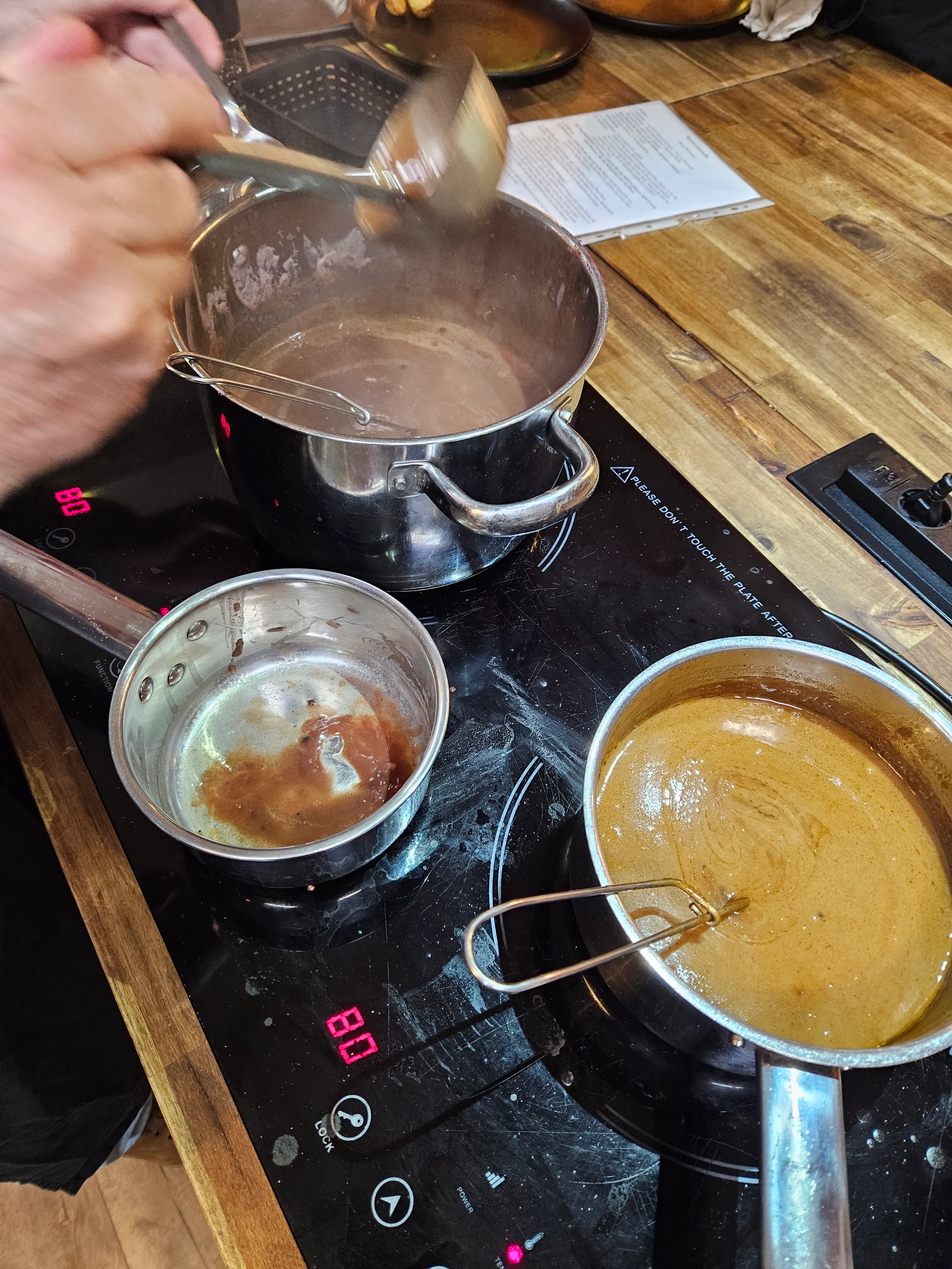 Person stirring sauce in multiple pots on stove.