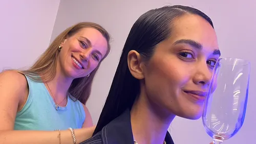 Zwei Frauen, eine lächelt, Glas haltend, drinnen.