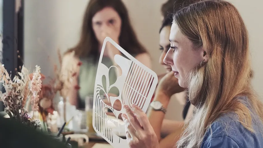 Woman holds decorative stencil in workshop setting.
