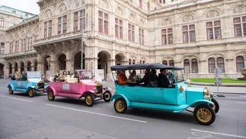 Three vintage cars driving past historic building.