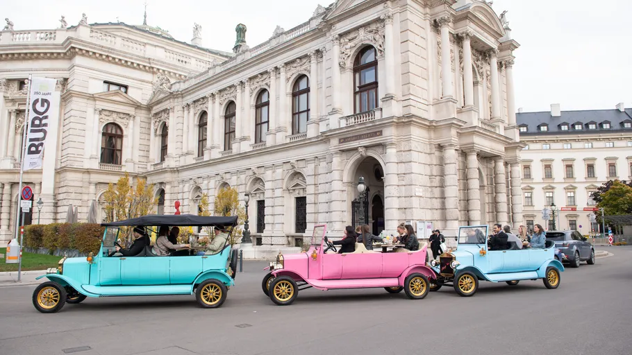 Oldtimer fahren an historischem Gebäude vorbei.
