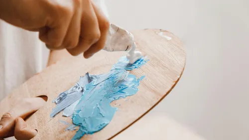 Hand squeezing paint onto wooden artist palette.