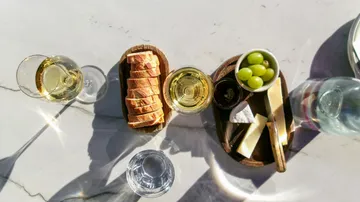 Brot, Käse, Wein und Trauben auf einem Tisch.