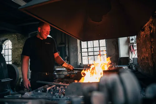 Blacksmith smiling while working with forge fire.