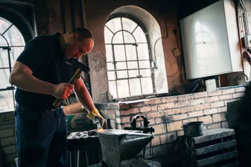 Schmied hämmert Metall auf Amboss in Werkstatt.