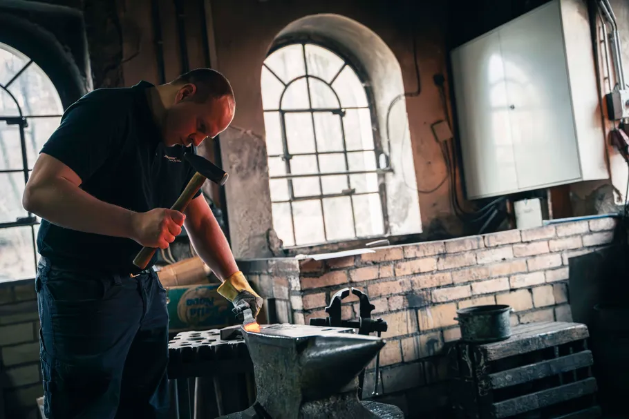 Blacksmith hammering metal on anvil in workshop.