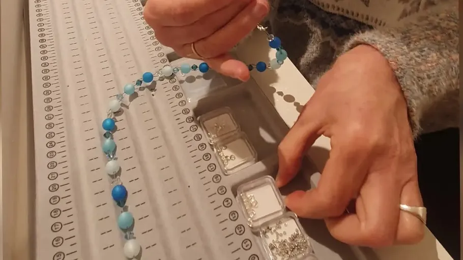 Hands arranging blue beads on beading board.
