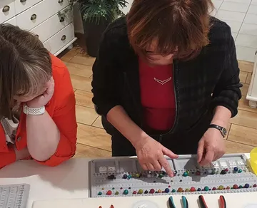 Zwei Frauen ordnen Perlen auf Tabletts drinnen.