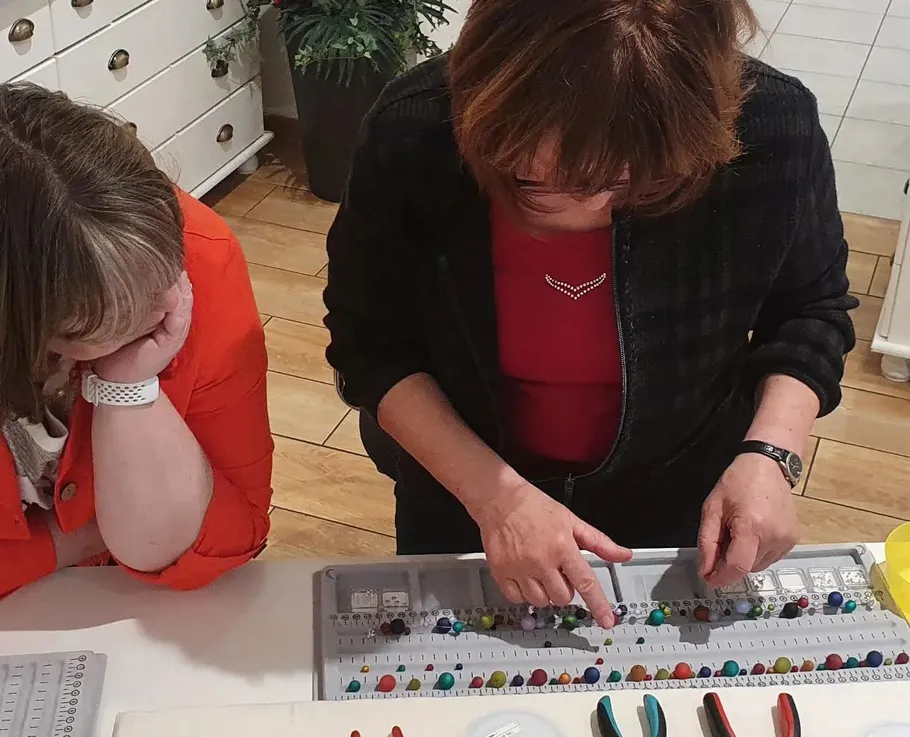 Two women organizing beads on trays indoors.
