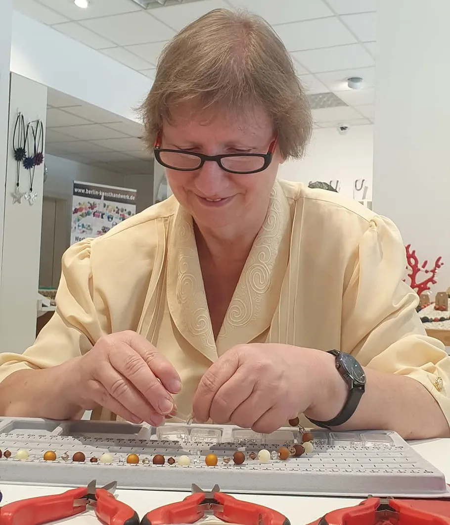 Person smiling while making jewelry indoors.