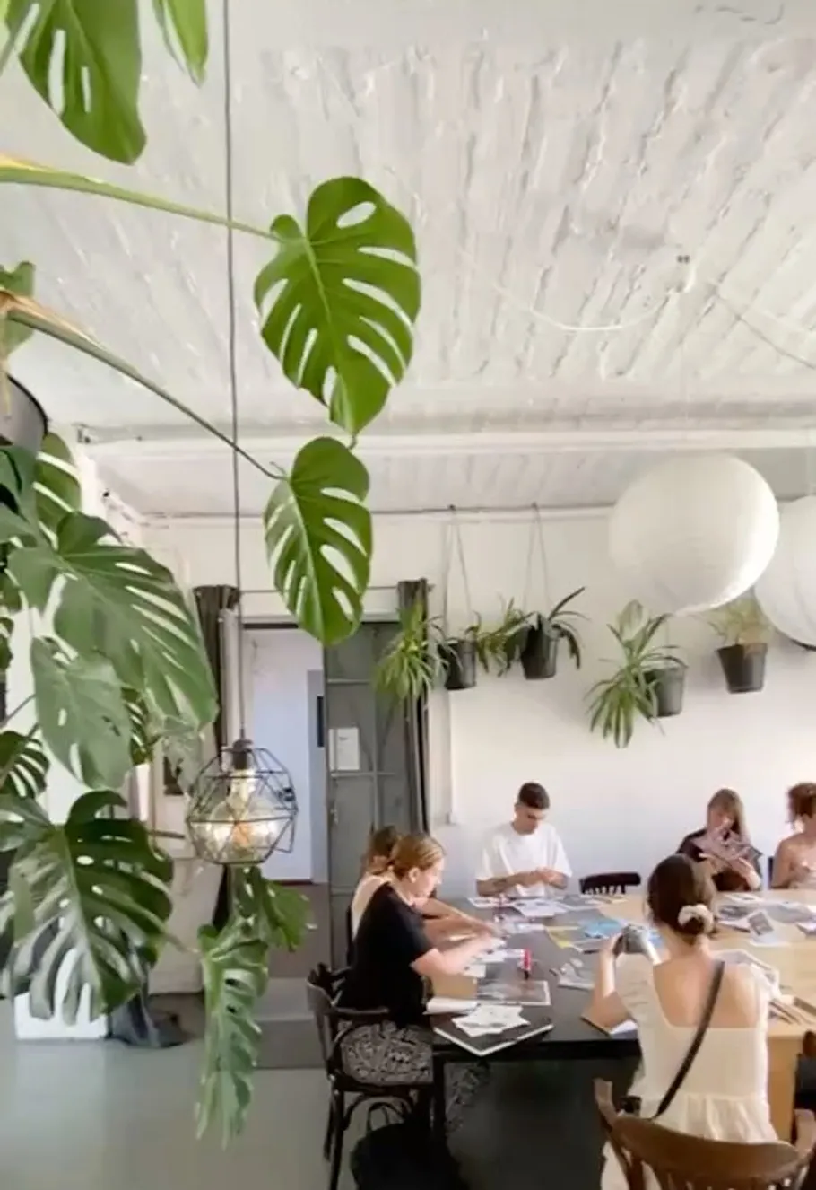 People crafting at a table in plant-filled room.
