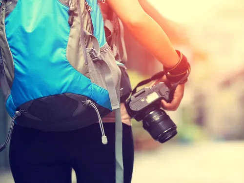 Person with backpack holds camera in an urban environment.