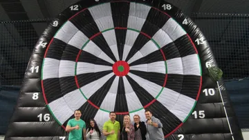 Gruppe von fünf vor riesiger Dartscheibe.