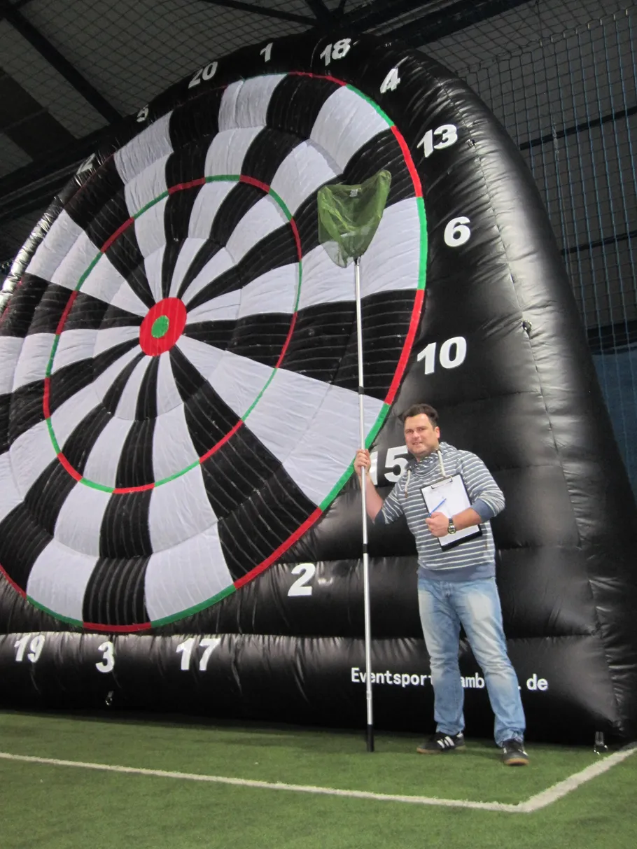Man standing by giant inflatable dartboard indoors.