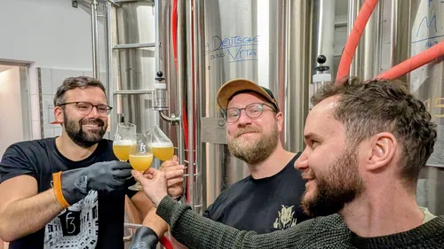 Three men toasting with beer in brewery.